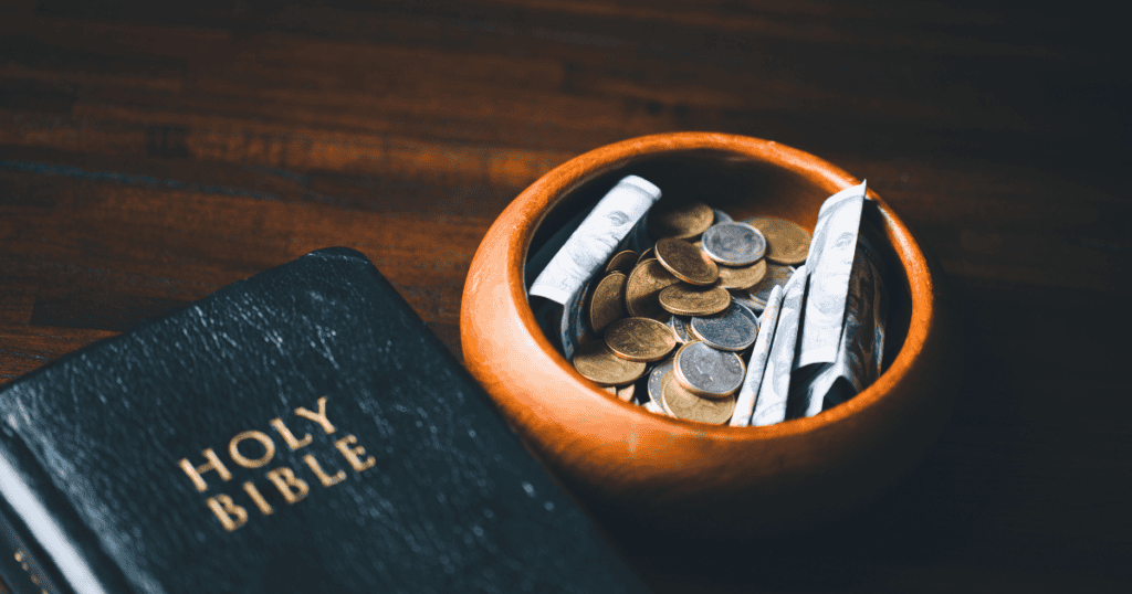 A dark book titled “HOLY BIBLE” rests on a table beside a small orange bowl filled with gold coins and scattered bills.